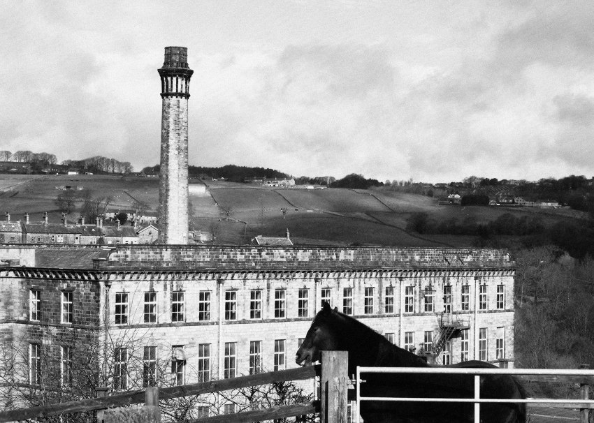 A mill against hills, watched by a horse.