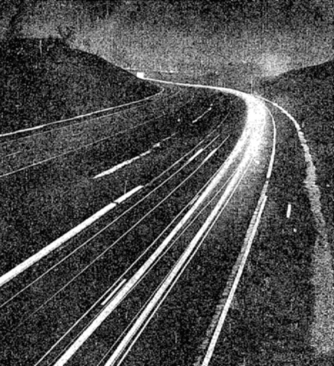 A low resolution image of streaks of light on a curving road.
