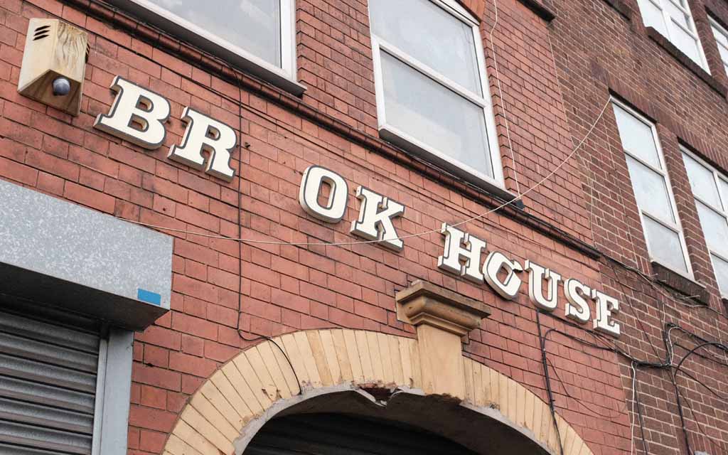A sign on an industrial building in Birmingham. It reads 'Brook House' except one O is missing and another is broken and hanging loose.