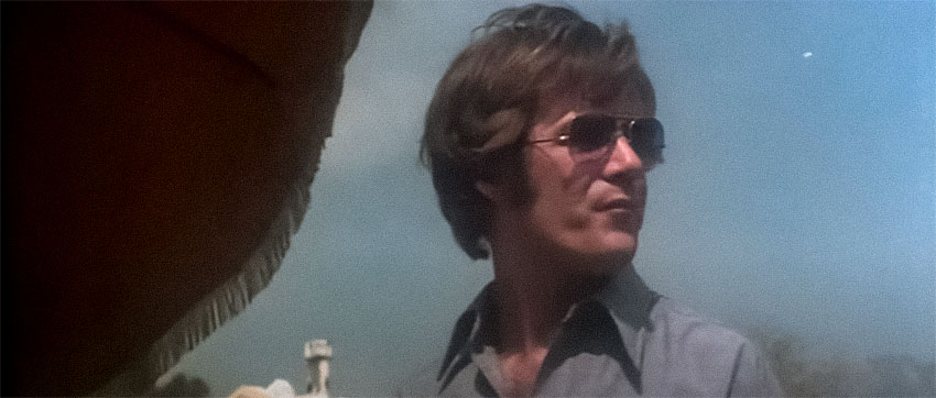 A screengrab from The Todd Killings showing Skipper Todd with bushy long hair, shades, and a wide collared shirt.