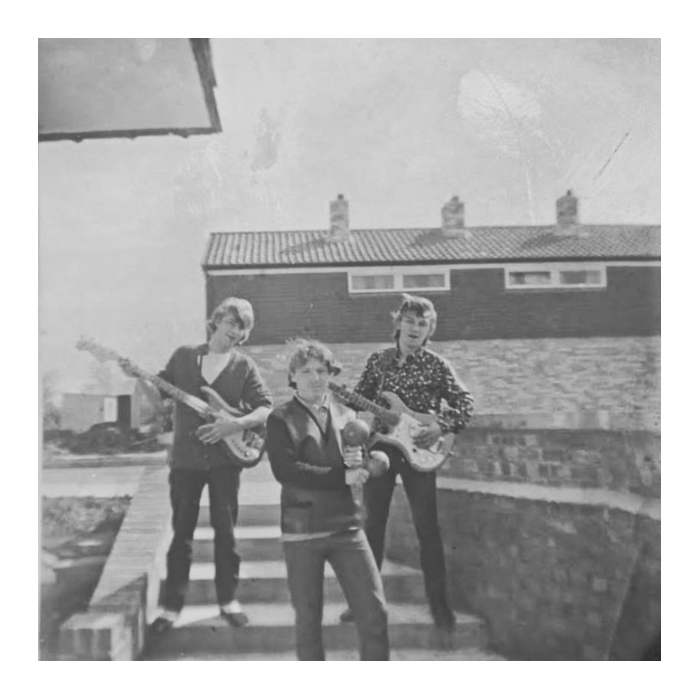 Three young men on the steps of a 1960s council house. One has a guitar, one has a bass guitar, and one is holding maracas. They're dressed in typical 1960s style.