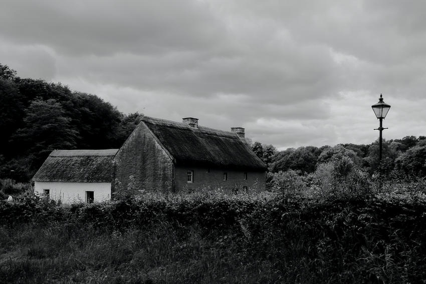 Some old cottages next to a Victorian lamppost in a rural setting, under a moody sky.