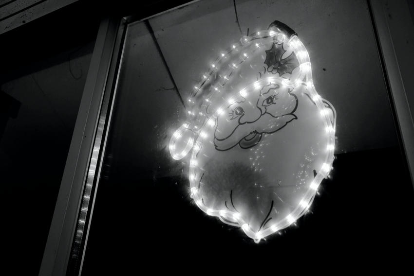 A Christmas decoration in the darkened window of a farm building – the smiling face of Father Christmas surrounded by fairy lights.