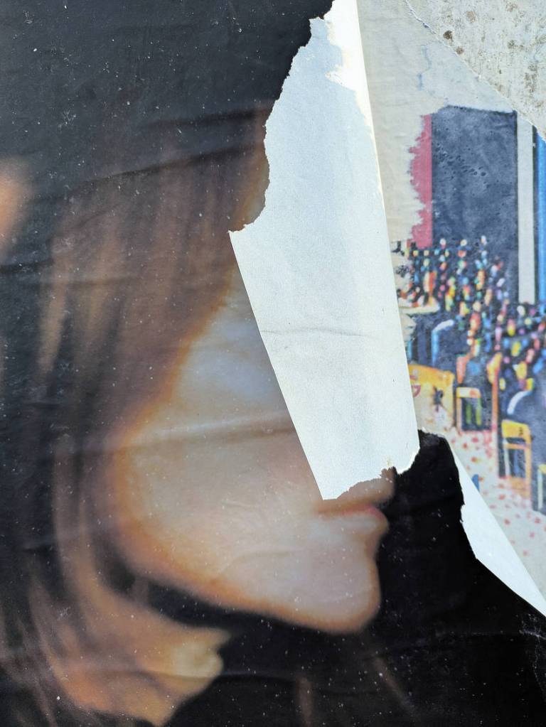 A poster with a woman in profile. It's been torn so that a flap of paper conceals her face rendering it blank and inscrutable.