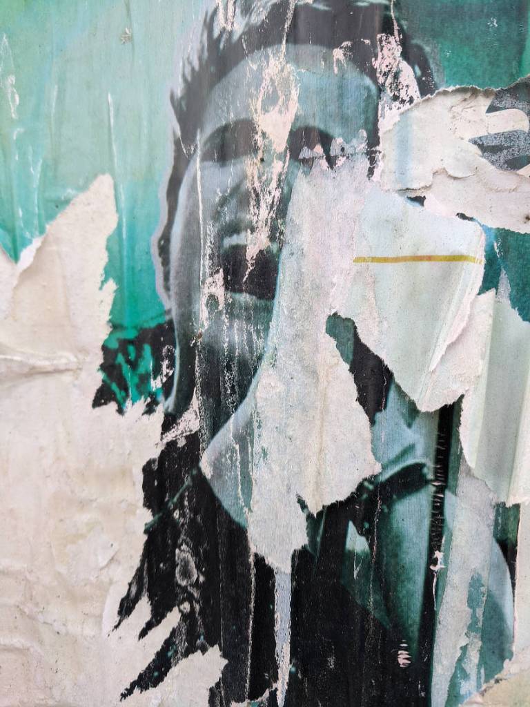 A ripped, faded poster which appears to show someone singing, only now their eyes are blank and it looks more like they're screaming.