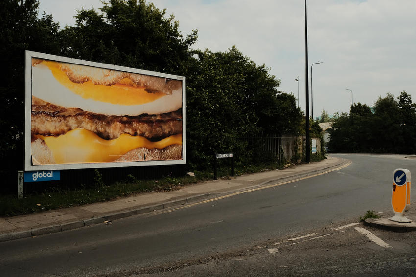 The corner of a road on an industrial estate with a billboard advertising a McDonald's breakfast sandwich.