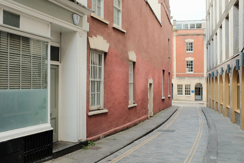 A side street lined with 18th century buildings on one side and a modern hotel on the other. There are no people.