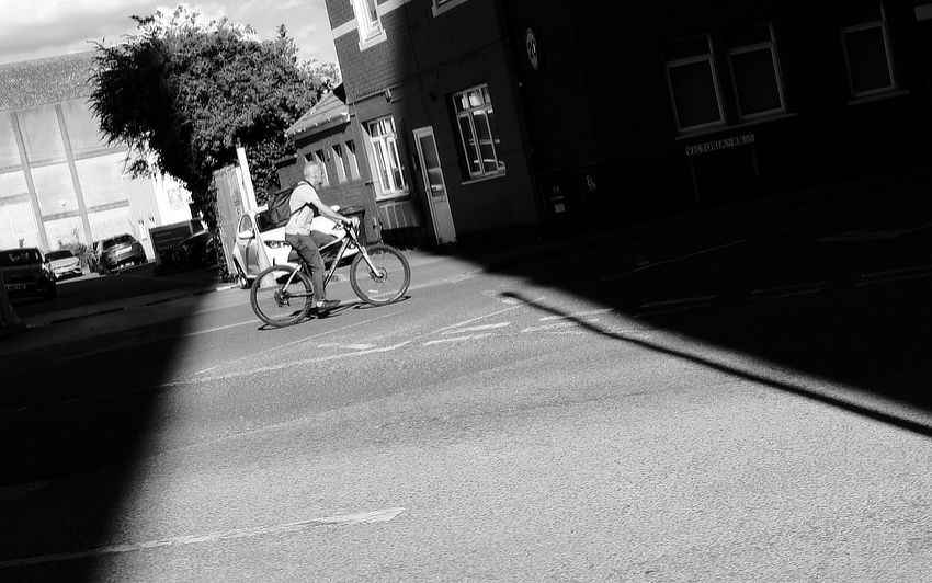 A black and white photo of someone cycling through a ray of sunlight on an industrial estate.
