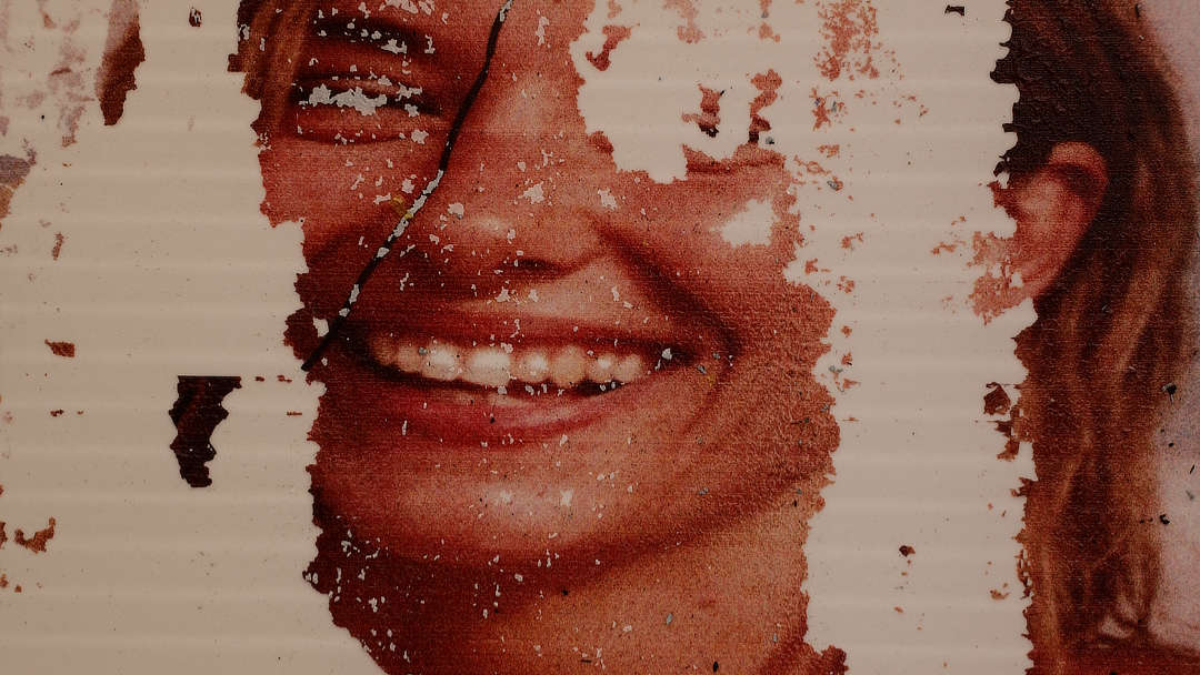 A decaying poster with a grimacing face mostly torn and eaten away.