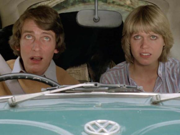A young man and a young man in turquoise Volkswagen are looking shocked at something.