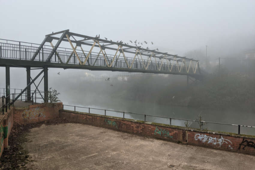 A metal bridge covered in pigeons disappearing into mist.