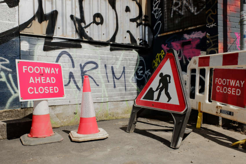 Temporary signs warn that the footway ahead is closed. There are plastic barriers and roadworks signs.