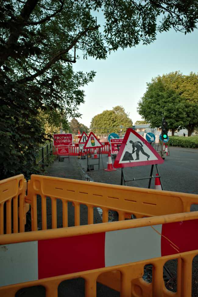A comprehensively blocked road and pavement cluttered with signs, barriers, temporary lights and railings.
