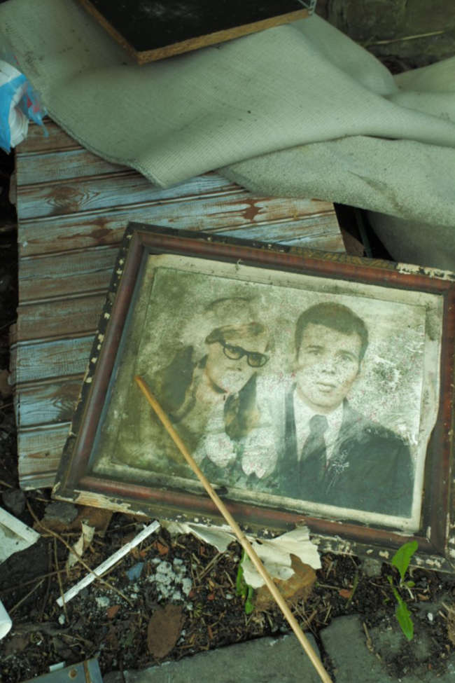 A pile of illegally dumped waste. On top is a mouldy framed portrait of a couple, perhaps on their wedding day, in about 1970.