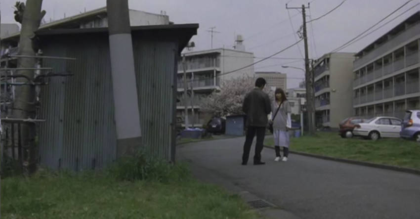 A street between apartment blocks with bland grey structures, white and grey cars, and a general sense of mundane reality.