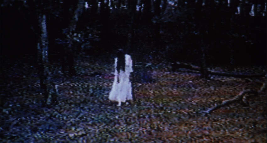 A grainy video image of a girl with long hair and a white nightdress.