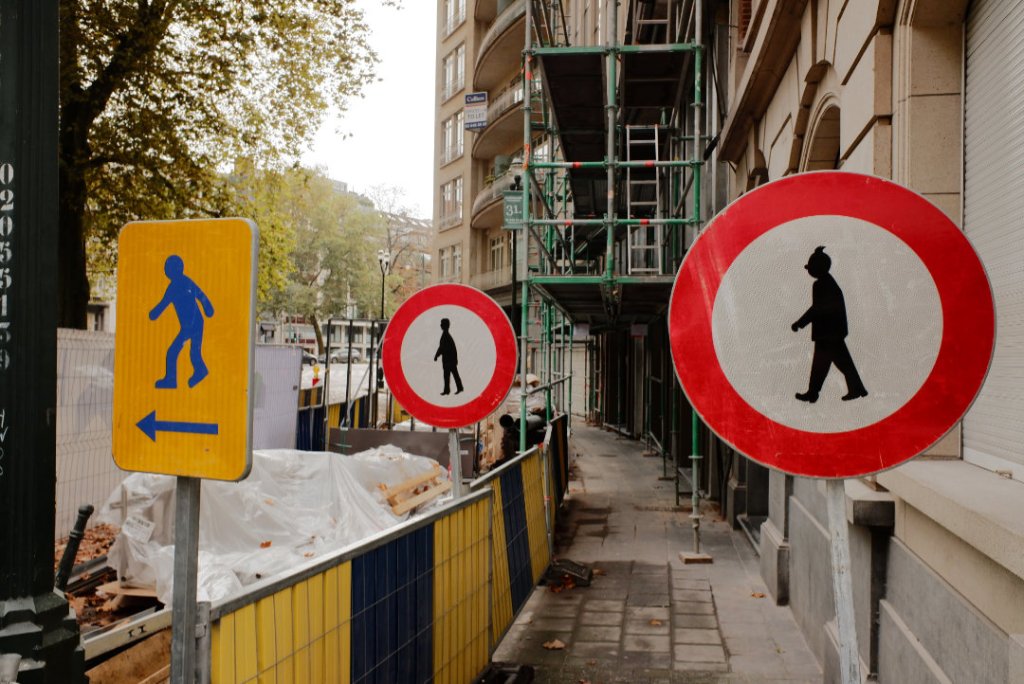 A chaotic pavement in Brussels with barriers and scaffolding. One of the warning signs features a silhouette of Tintin.