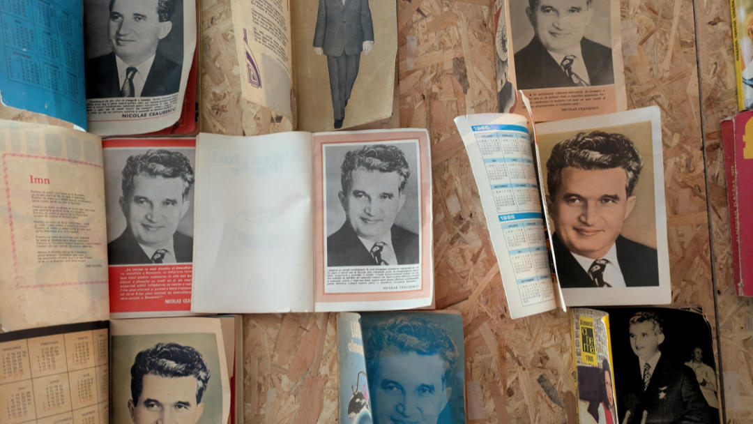 A wall covered with official portraits of Nicolae Ceaușescu from magazines and schoolbooks.
