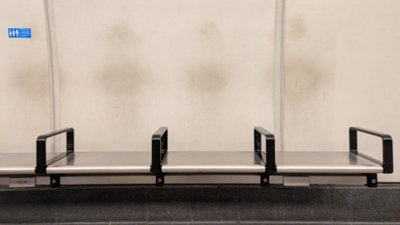 A bench on the London Underground with dirty smudges on the wall showing where people have been sitting.